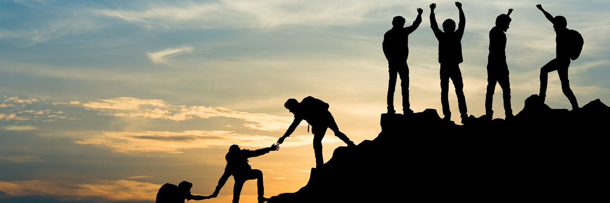 Team of people helping each other up a clif